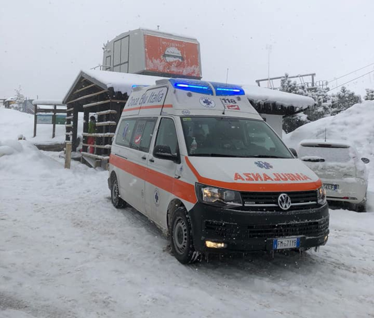 Ambulanza Volkswagen 4x4 della Croce Blu di Trivero con luci accese, parcheggiata su una strada innevata in un contesto montano. Si vedono edifici e alberi coperti di neve sullo sfondo.