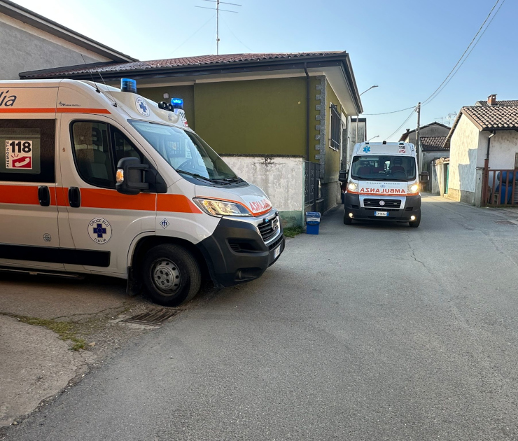 Due ambulanze 118 Croce Blu Italia Fiat Ducato bianche con banda arancione e scritte "AMBULANZA" durante servizio su strada urbana nel vercellese. Mezzi con lampeggianti blu attivi, adesivi 118 visibili, contesto residenziale con case a uno e due piani.
