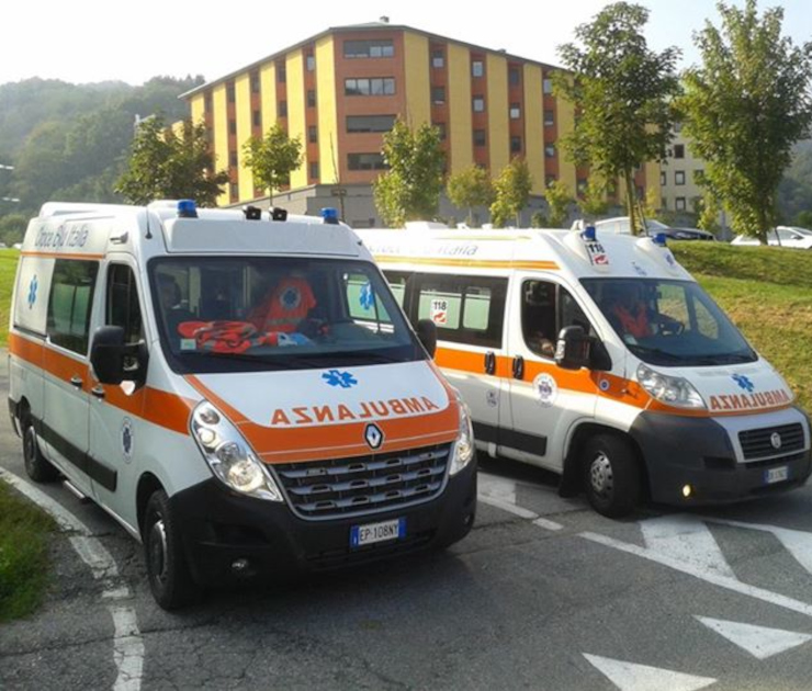 Due ambulanze della Croce Blu Italia parcheggiate davanti all'ingresso dell'Ospedale SS. Pietro e Paolo di Borgosesia, un moderno edificio a strisce gialle verticali. In primo piano ambulanza Renault Master, sullo sfondo ambulanza Fiat Ducato, entrambe bianche con banda arancione laterale e scritta "AMBULANZA".