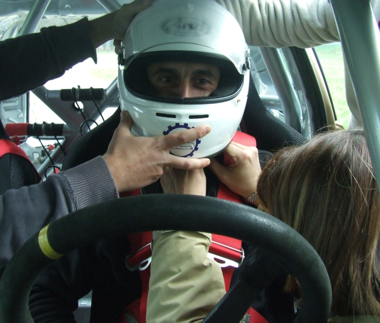 Volontari Croce Blu Italia durante esercitazione di estricazione di un pilota con casco integrale dall'abitacolo di un'auto da competizione dotata di roll-bar e cinture racing. Operatori applicano tecniche di immobilizzazione cervicale all'interno del veicolo sportivo.